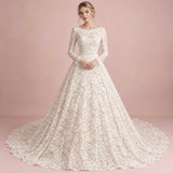 A woman modeling a long-sleeve lace ball gown with a full skirt and train against a soft pink studio backdrop.