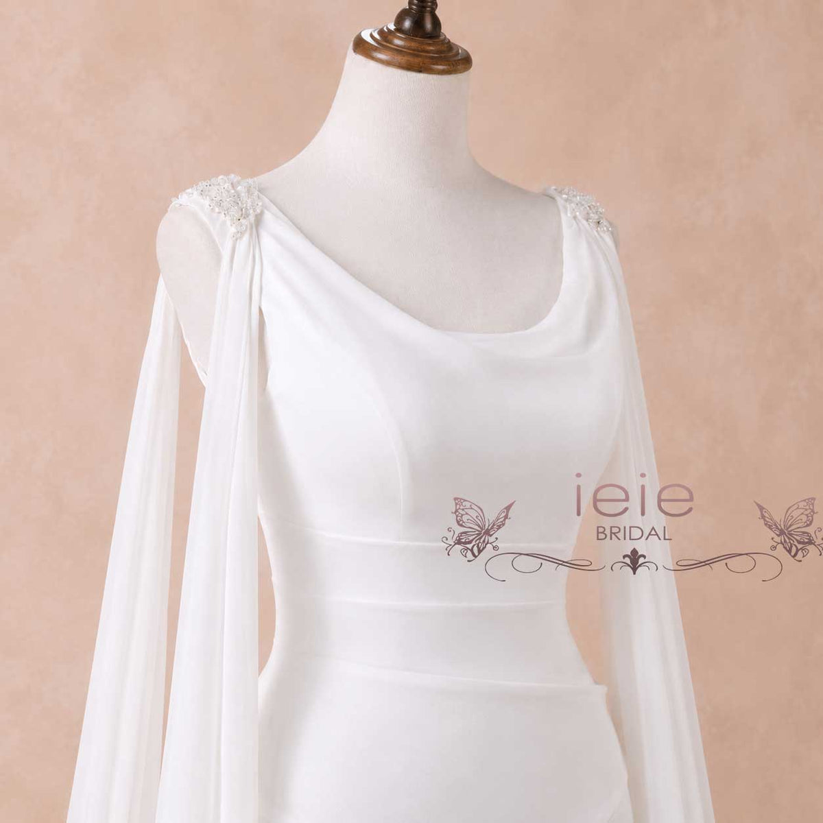 White bridal gown on a mannequin with draped sheer sleeves and embellished shoulder details, shown against a soft beige background. The brand name 'ieie BRIDAL' is watermarked on the front.